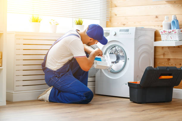 working man plumber repairs a washing machine in the laundry